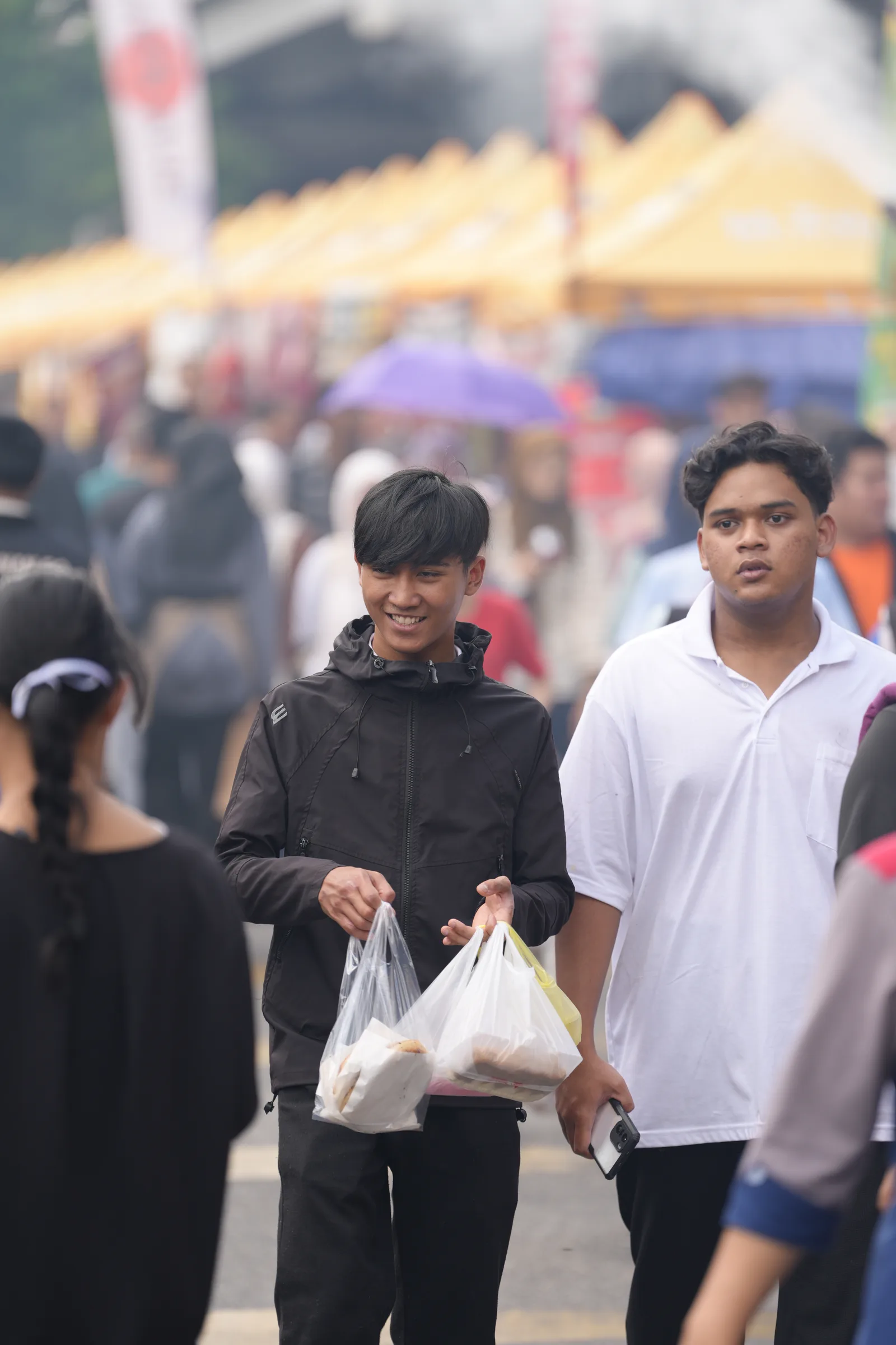 Two friends carrying iftar bags through the smoky bazaar crowd