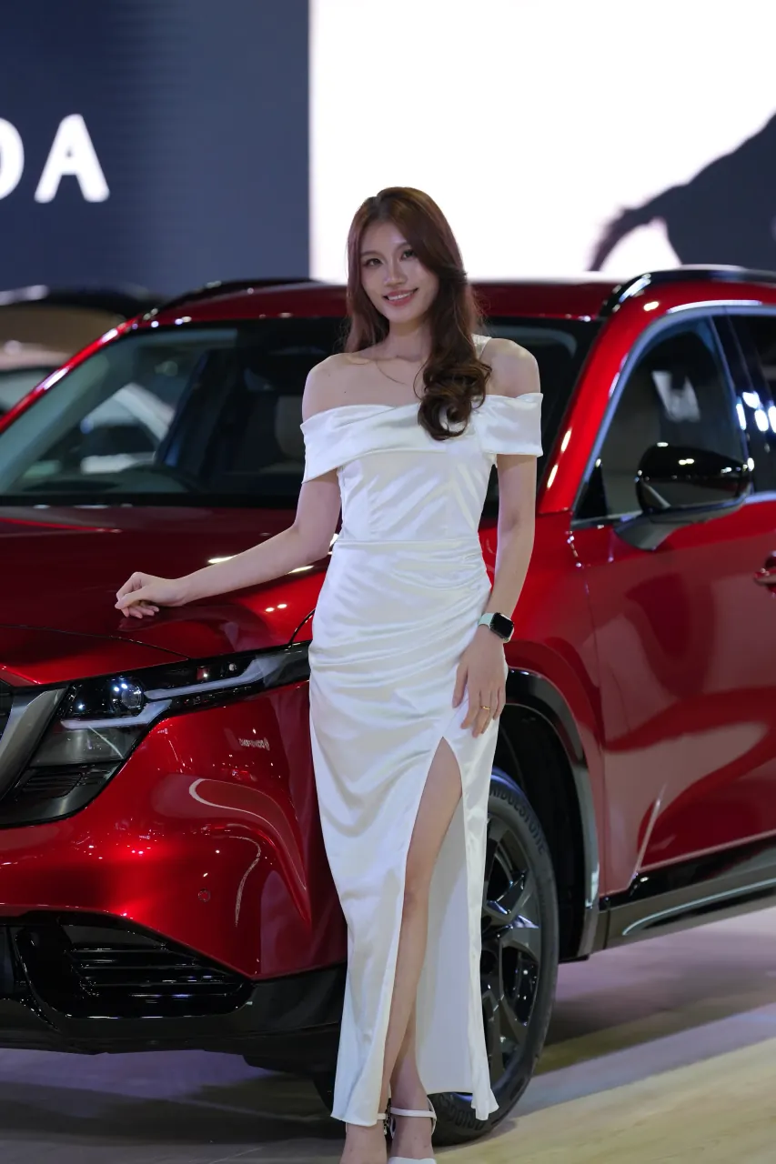 Presenter beside a red Mazda under the stand lighting