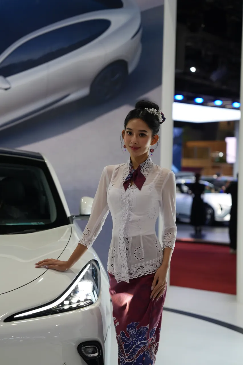 Presenter in traditional kebaya alongside a white sedan