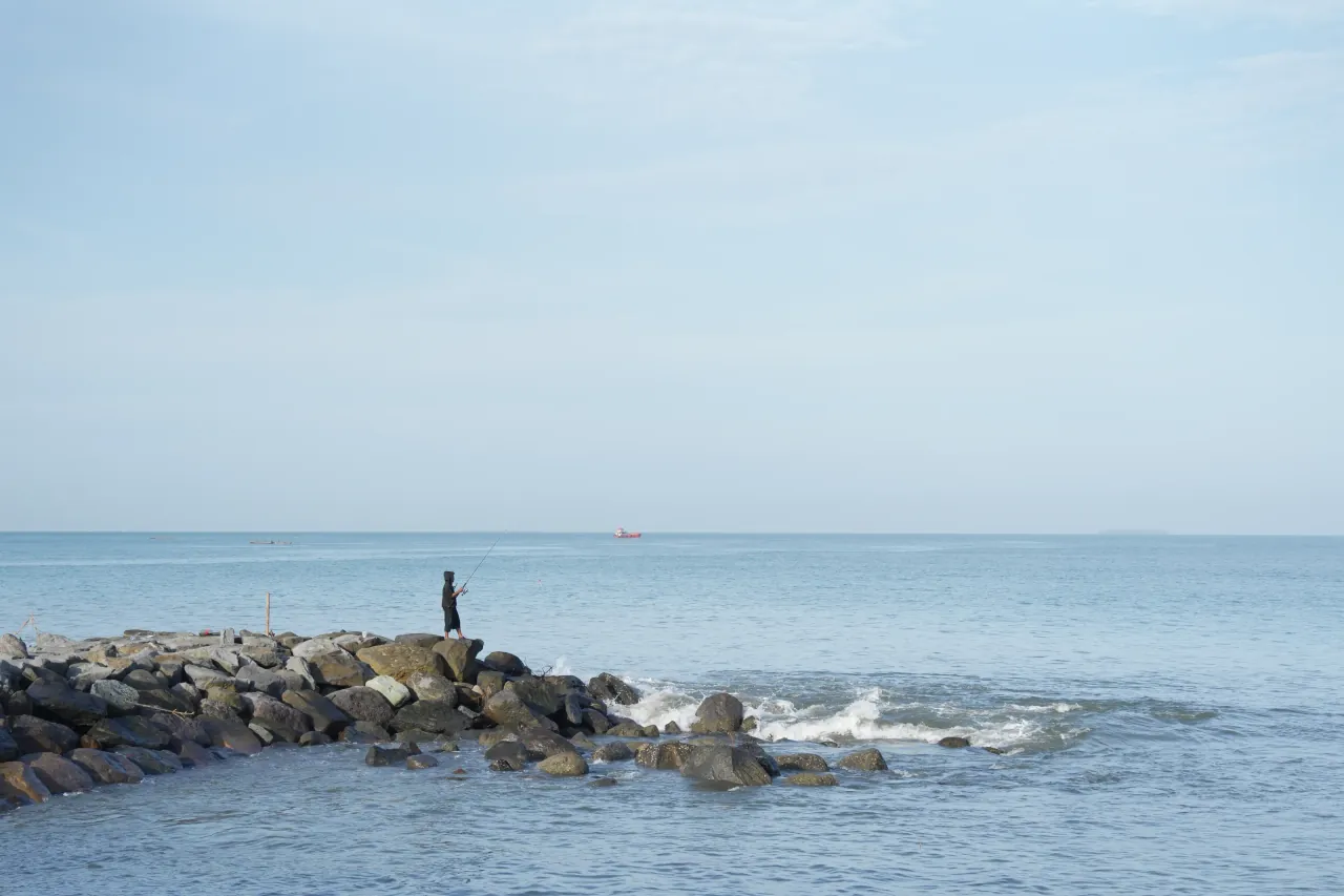 Lone fisherman on a rocky jetty — minimalist coastal photography, Padang